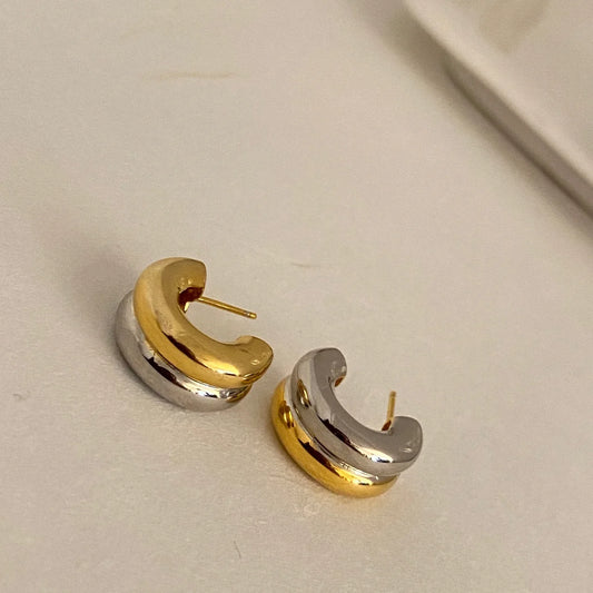 Paar klobige Bi-Color Creolen-Ohrstecker aus vergoldetem Messing und Silber, liegend auf einer hellen Fläche.