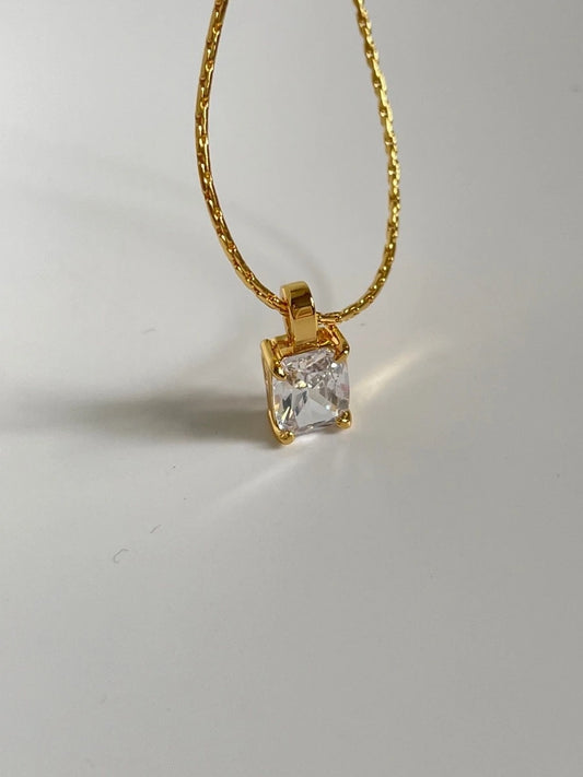Nahaufnahme einer goldenen Gliederkette mit einem funkelnden, rechteckigen Zirkonia-Anhänger im Smaragdschliff vor weißem Hintergrund.