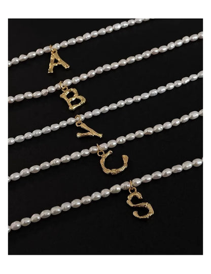 Süßwasserperlenketten mit verschiedenen vergoldeten Buchstaben-Anhängern (A, B, C, S) auf schwarzem Grund.