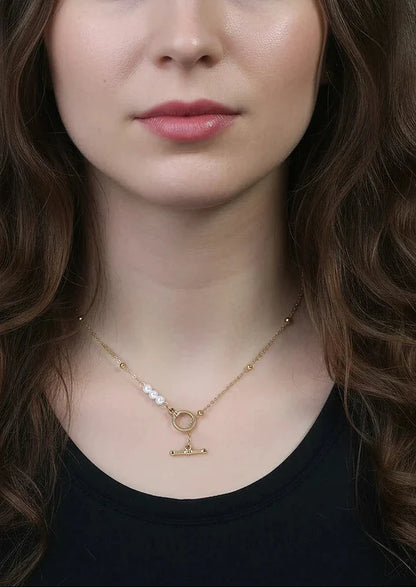 Eine Frau trägt die vergoldete Edelstahl-Kette mit Knebelverschluss und Muschelperlen zum schwarzen Oberteil.