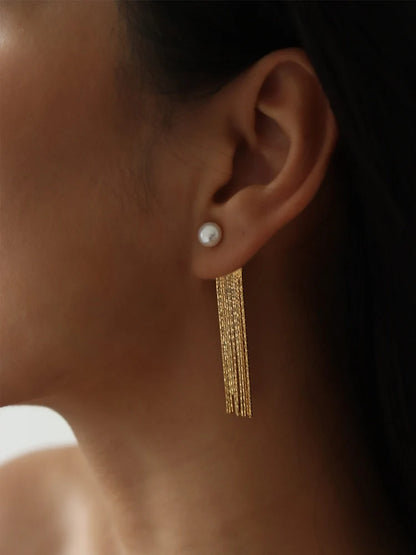 Seitliche Nahansicht einer Frau, die einen eleganten Ohrring trägt; eine weiße Süßwasserperle sitzt auf dem Ohrläppchen, von der ein langer, fächerartiger Besatz aus feinen, 14k vergoldeten Messingketten herabhängt.