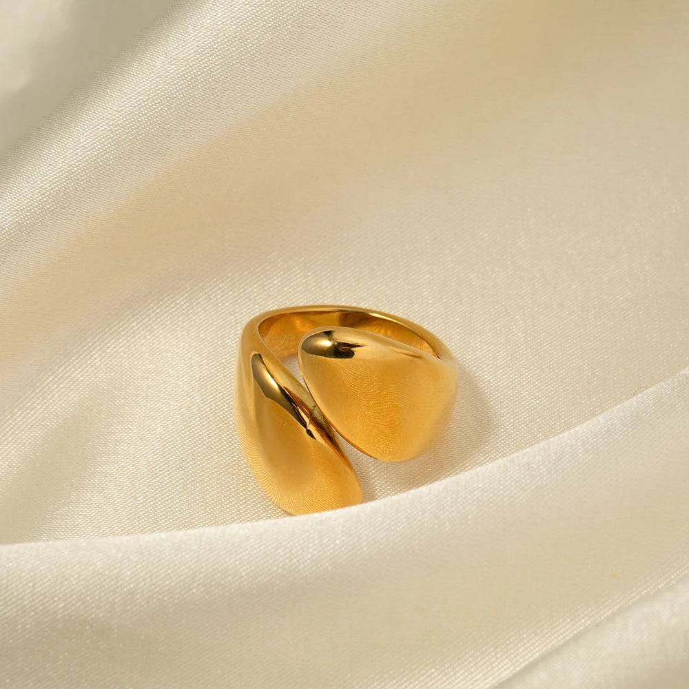 Nahaufnahme eines offenen, asymmetrischen Edelstahlrings mit einer 18K Gold Vergoldung, präsentiert auf einem hellen, seidig strukturierten Stoffhintergrund, der die glänzende Oberfläche hervorhebt.