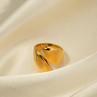 Nahaufnahme eines offenen, asymmetrischen Edelstahlrings mit einer 18K Gold Vergoldung, präsentiert auf einem hellen, seidig strukturierten Stoffhintergrund, der die glänzende Oberfläche hervorhebt.