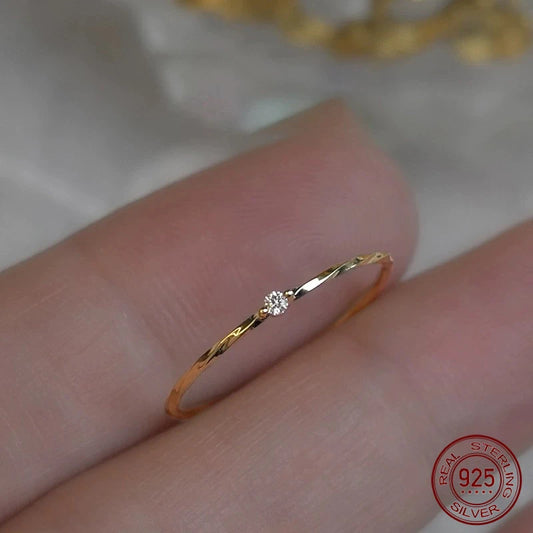 Nahaufnahme eines zarten, 18K Gold Platin vergoldeten 925 Silber Rings mit einer kleinen Zirkonia-Steinbesetzung. Der Ring hat eine leicht gedrehte/verwundene Schiene und liegt auf einem Finger. Ein 925 Sterling Silber-Stempel (rot) ist in der Ecke sichtbar.