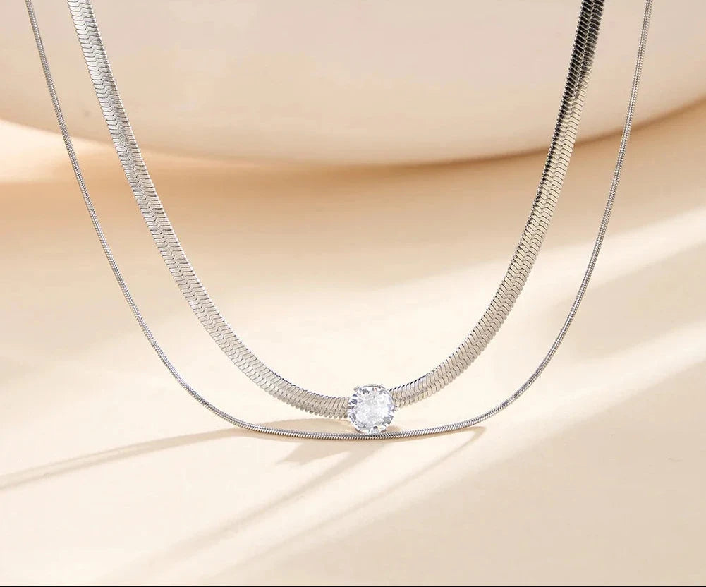 Nahaufnahme der zweireihigen silberfarbenen Edelstahl-Kette mit flacher Schlangenstruktur und Zirkonia-Solitär.