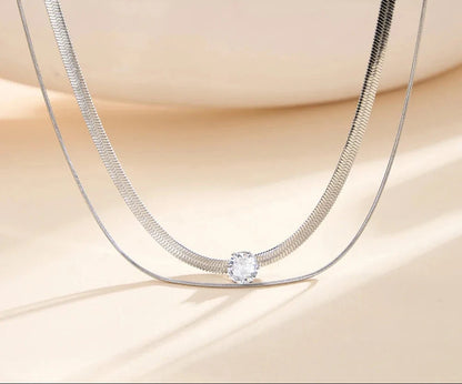 Nahaufnahme der zweireihigen silberfarbenen Edelstahl-Kette mit flacher Schlangenstruktur und Zirkonia-Solitär.