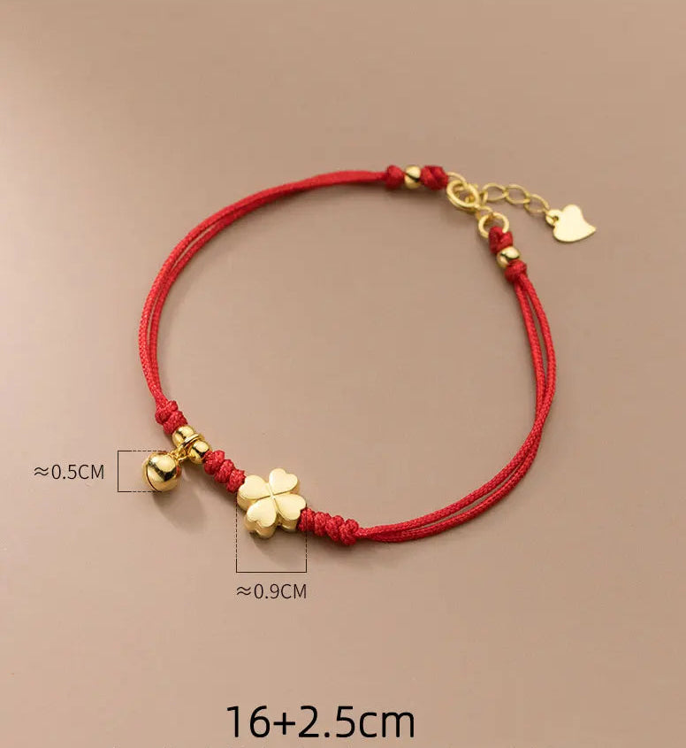Schlichte Produktansicht des verstellbaren roten Textilarmbands mit vergoldetem Kleeblatt und Glöckchen.