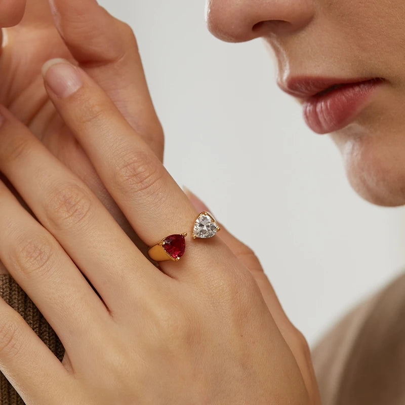 Zwei Frauenhände tragen jeweils einen 18K vergoldeten Ring mit Herzsteinen (rot und klar), Partnerringe