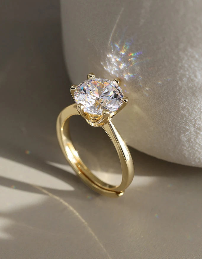 Eleganter, verstellbarer Goldring aus 14K vergoldetem 925er Sterling Silber, mit einem großen, funkelnden Zirkonia-Stein in Krappenfassung, der im Sonnenlicht glänzt. Das Logo "Orsen Jewels" ist oben links sichtbar.