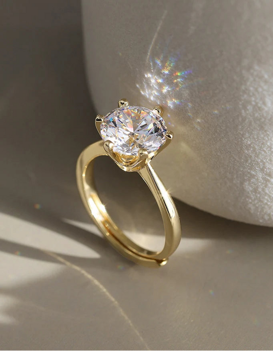 Eleganter, verstellbarer Goldring aus 14K vergoldetem 925er Sterling Silber, mit einem großen, funkelnden Zirkonia-Stein in Krappenfassung, der im Sonnenlicht glänzt. Das Logo "Orsen Jewels" ist oben links sichtbar.