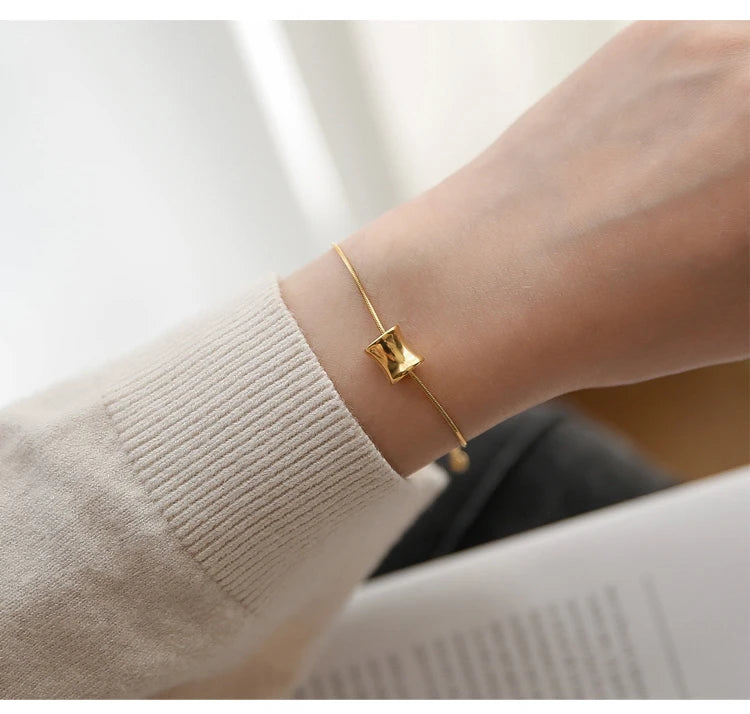 Filigranes 18K vergoldetes Titan-Armband mit gebogenem Zylinder-Anhänger am Handgelenk einer Frau.