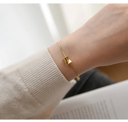 Filigranes 18K vergoldetes Titan-Armband mit gebogenem Zylinder-Anhänger am Handgelenk einer Frau.