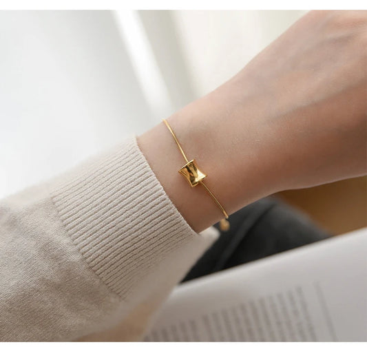 Filigranes 18K vergoldetes Titan-Armband mit gebogenem Zylinder-Anhänger am Handgelenk einer Frau.