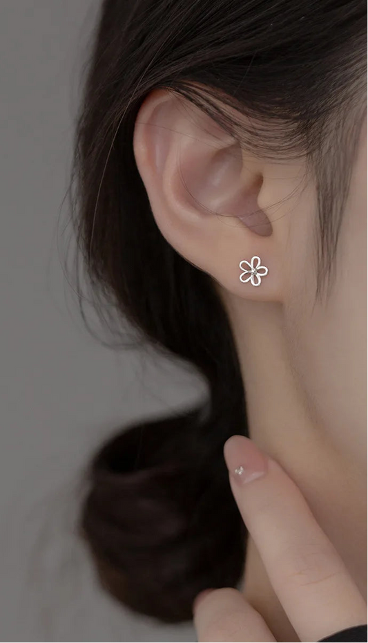 Model präsentiert den kleinen, silbernen Blumen-Ohrstecker dezent am Ohrläppchen.