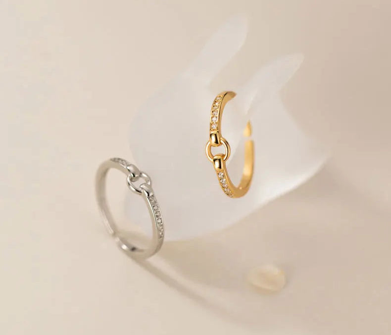 Der filigrane Zirkonia-Ring in zwei Ausführungen: Einmal in reinem 925er Silber und einmal mit 18K Gelbgold-Vergoldung, elegant auf einem weißen Halter arrangiert.