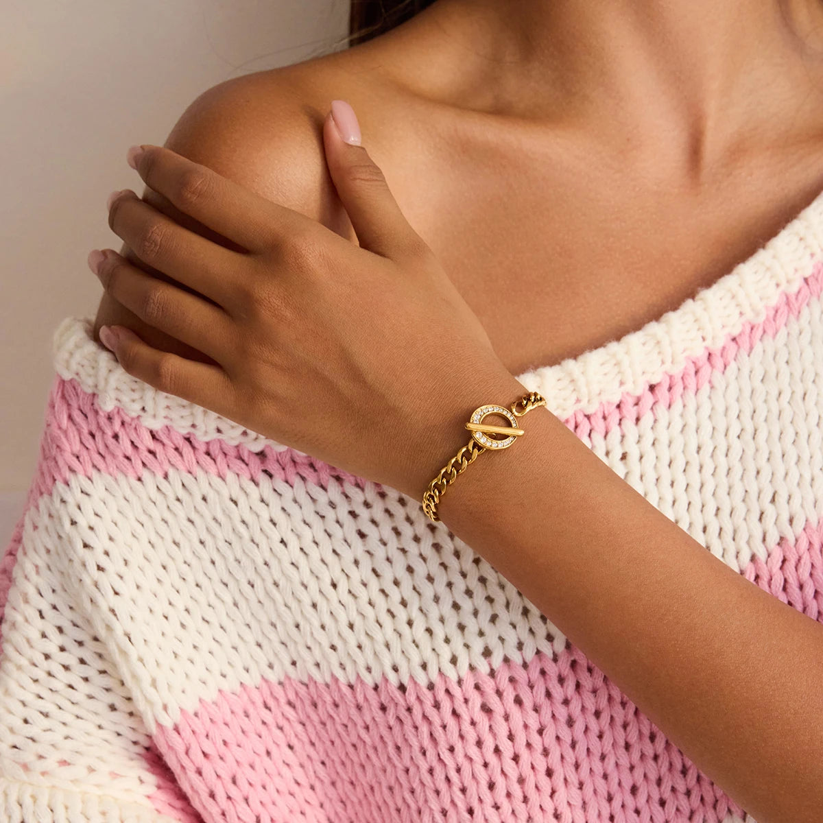 Eine Frau trägt das goldene Panzerarmband mit Zirkonia-Details zu einem gestreiften Strickpullover, um den modernen Alltagslook des Schmuckstücks zu präsentieren.