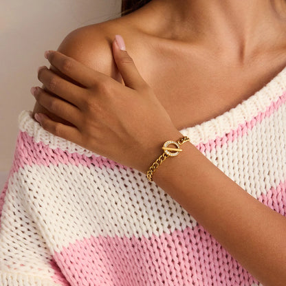 Eine Frau trägt das goldene Panzerarmband mit Zirkonia-Details zu einem gestreiften Strickpullover, um den modernen Alltagslook des Schmuckstücks zu präsentieren.