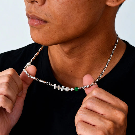 Nahaufnahme eines Mannes, der eine asymmetrische Edelstahlkette mit integrierten Metallperlen, einer weißen Süßwasserperle und einer grünen Jade-Perle trägt.