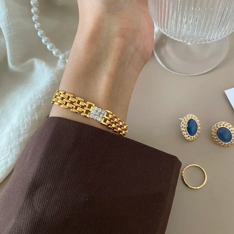 Nahaufnahme am Handgelenk einer Frau mit einem breiten, 18K vergoldeten Messing-Gliederarmband und zentralem Zirkonia-Steinbesatz.