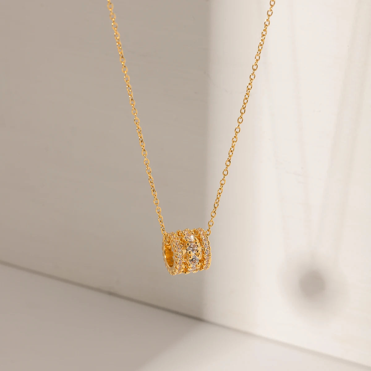 Nahaufnahme einer Halskette aus 18K goldvergoldetem Edelstahl; der Anhänger ist ein kleiner, eleganter Zylinder, der rundum dicht mit funkelnden, klaren Zirkoniasteinen besetzt ist.