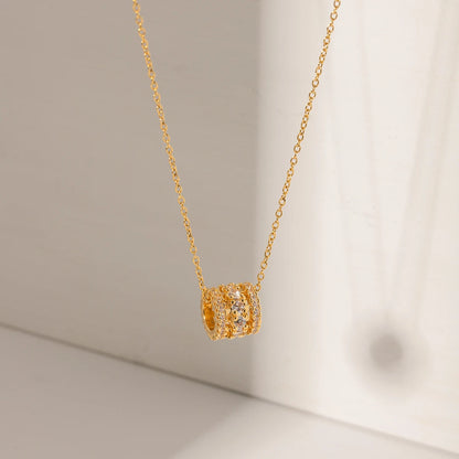 Nahaufnahme einer Halskette aus 18K goldvergoldetem Edelstahl; der Anhänger ist ein kleiner, eleganter Zylinder, der rundum dicht mit funkelnden, klaren Zirkoniasteinen besetzt ist.