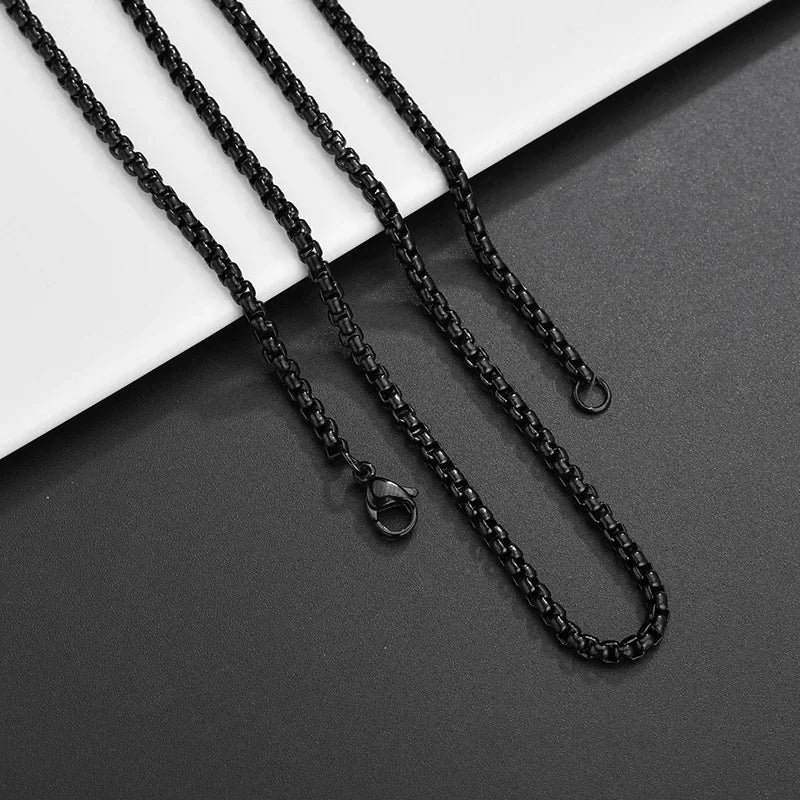 Drei schwarze Edelstahl-Boxketten in unterschiedlicher Länge, liegend auf einem schwarz-weißen Hintergrund.

