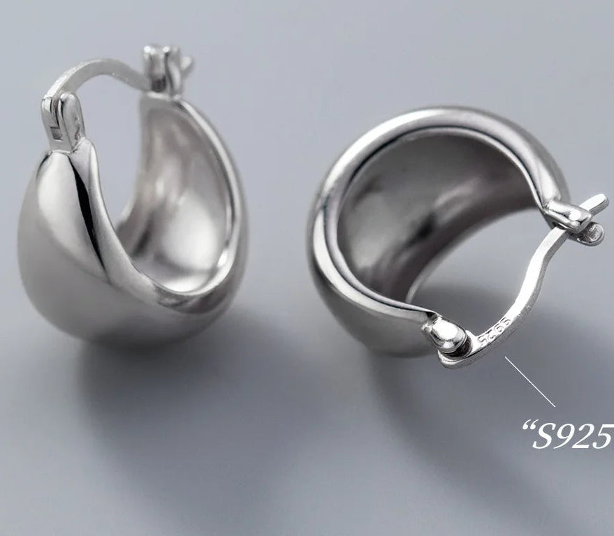 Zwei bauchige Creolen-Ohrringe aus 925er Silber auf grauem Hintergrund, einer von vorne und einer von der Seite, der die Hohlform des Ohrrings zeigt.