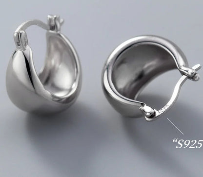 Zwei bauchige Creolen-Ohrringe aus 925er Silber auf grauem Hintergrund, einer von vorne und einer von der Seite, der die Hohlform des Ohrrings zeigt.