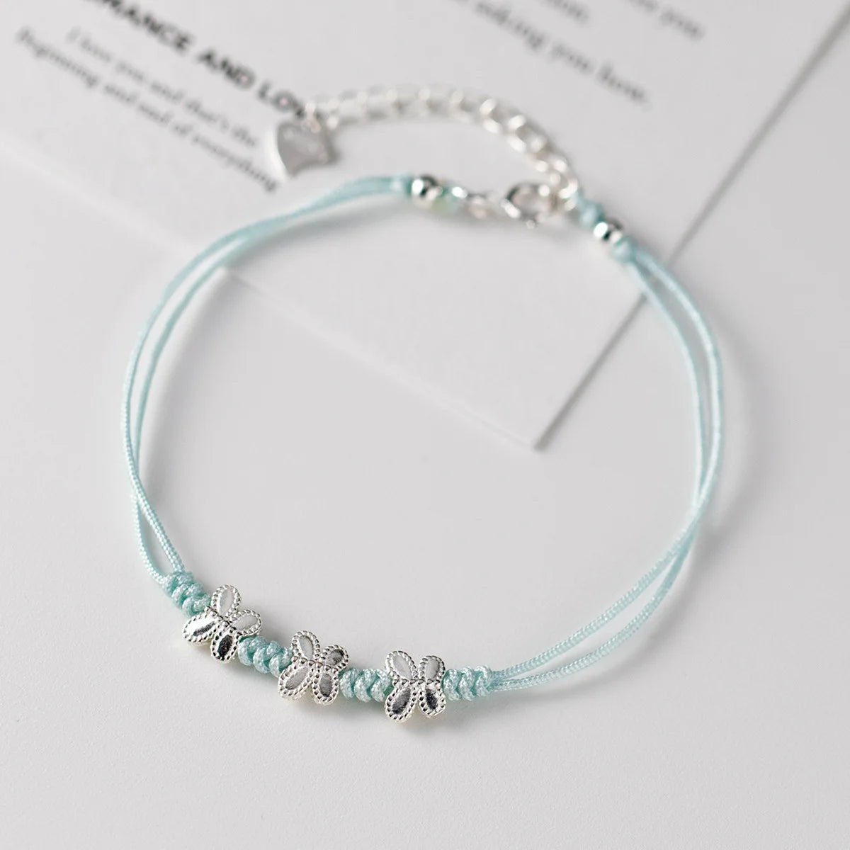 Hellblaues Kordelarmband mit drei Schmetterlingselementen aus 925er Sterling Silber elegant präsentiert.