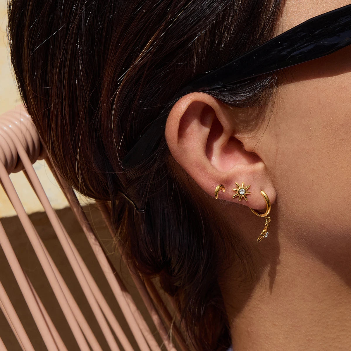 Eine Frau trägt drei kleine goldene Edelstahl-Ohrstecker mit 18K PVD-Vergoldung. Ein winziger Tropfen ist im ersten Ohrloch zu sehen, ein schlichter, kleiner Ohrstecker im zweiten und ein noch kleinerer im dritten.