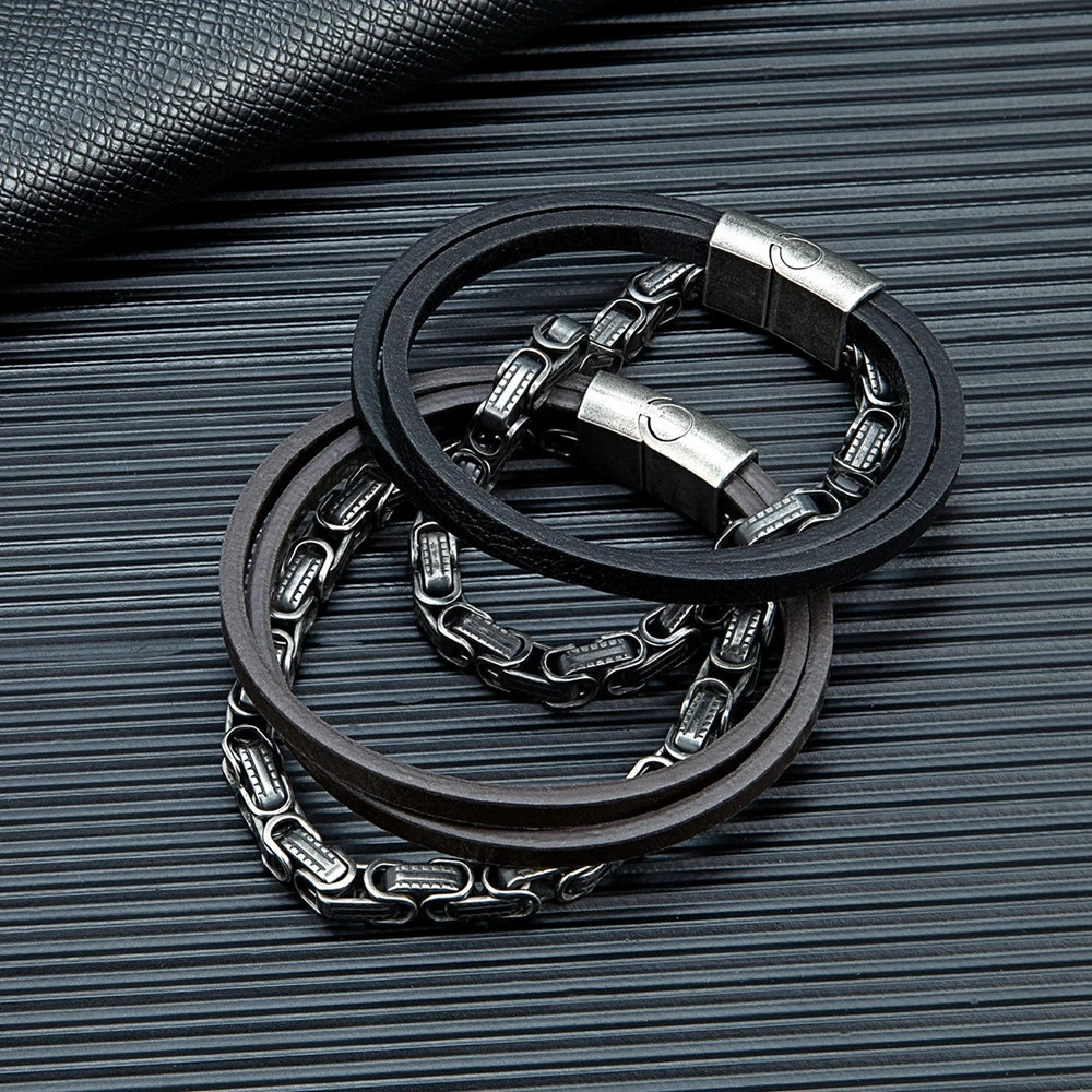 Die schwarze und braune Variante des mehrreihigen Königsketten-Lederarmbands nebeneinander arrangiert auf einer strukturierten, dunklen Oberfläche.
