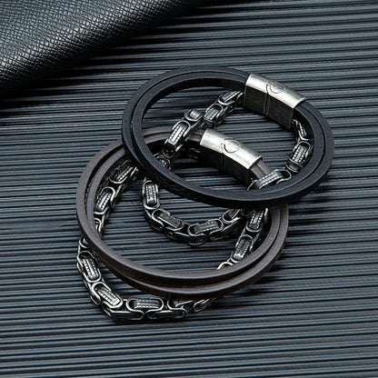 Die schwarze und braune Variante des mehrreihigen Königsketten-Lederarmbands nebeneinander arrangiert auf einer strukturierten, dunklen Oberfläche.