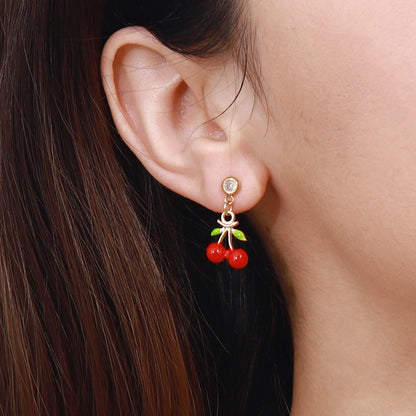 Modell trägt einen filigranen Kirschen-Ohrstecker aus vergoldetem Edelstahl mit einem kleinen Zirkonia-Stein und roten Kirsch-Anhängern am Ohrläppchen.