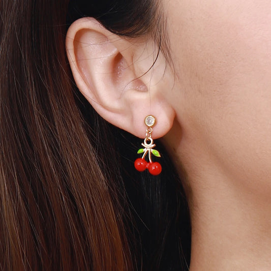 Modell trägt einen filigranen Kirschen-Ohrstecker aus vergoldetem Edelstahl mit einem kleinen Zirkonia-Stein und roten Kirsch-Anhängern am Ohrläppchen.