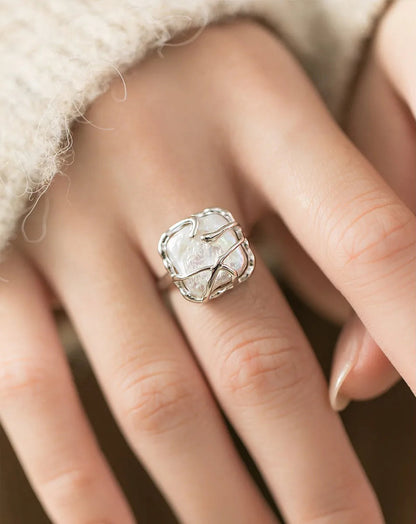 Nahaufnahme der Hand einer Frau, die einen auffälligen, offenen Ring aus 925er Silber mit einem unregelmäßigen, weißen Stein-Element im Wickel-Design trägt.

