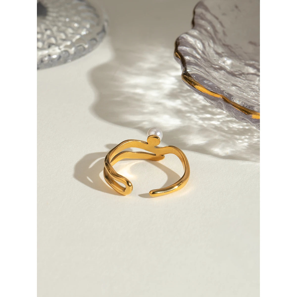 „Produktfotografie des offenen 18K Goldperlenrings auf klaren, architektonischen weißen Linien und Stufen, die das geometrische, aber weiche Design hervorheben.“
