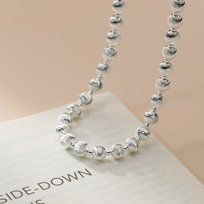Kugelperlen-Halskette aus 925er Sterling Silber (mattiert und glänzend), die spiralförmig auf einem Buch liegt und den verstellbaren Verschluss zeigt.