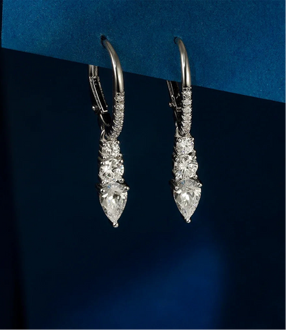 Freigestelltes Paar hängender Ohrringe aus reinem 925er Sterling Silber, jeweils besetzt mit drei gestuften, tropfenförmigen Zirkonia-Steinen und einem Zirkonia-besetzten Kreolenbügel. Das 'Real 925 Sterling Silver' Siegel ist unten rechts erkennbar.