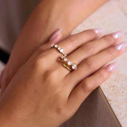 „Nahaufnahme einer Frauenhand mit gepflegten hellrosa Nägeln, die einen eleganten, offen gestalteten Ring aus 18K vergoldetem Edelstahl mit einer Reihe funkelnder Zirkonia-Steine trägt.“
