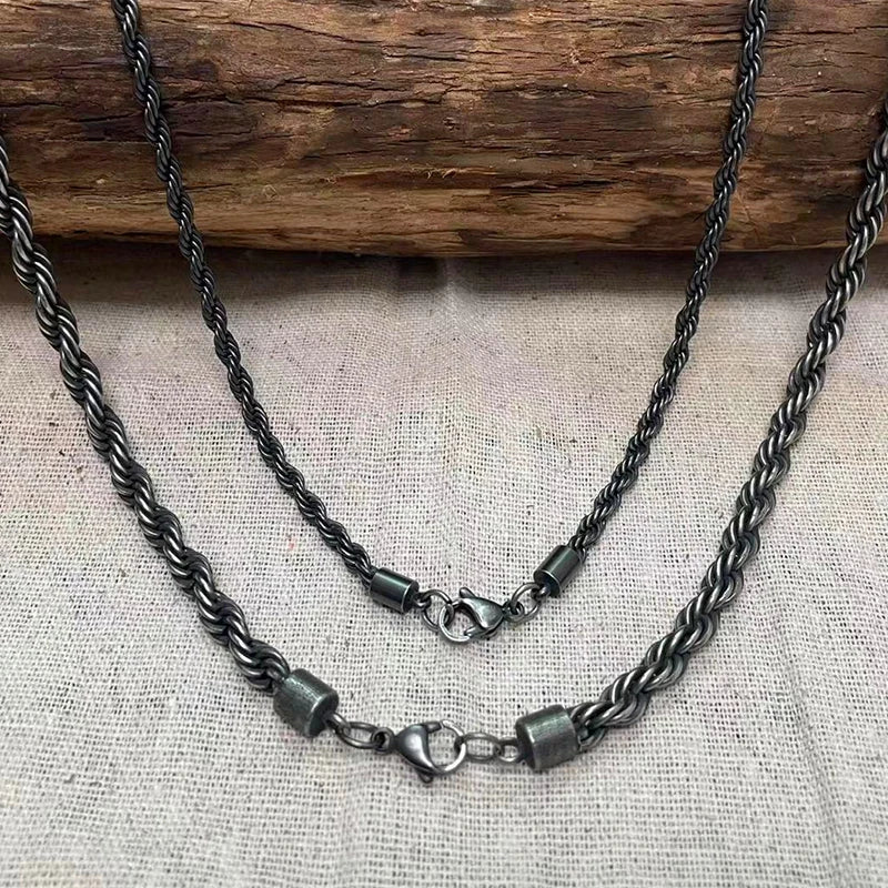 Zwei schwarze Edelstahl-Kordelketten in unterschiedlichen Längen (Lagen-Look) mit Karabinerverschlüssen, hängend vor einem hellen Hintergrund.