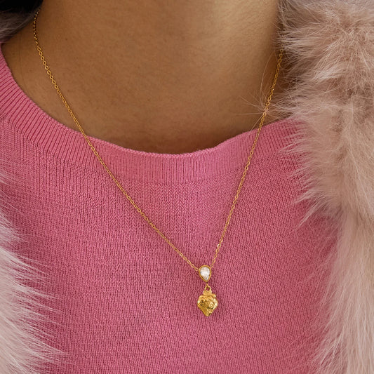 Nahaufnahme einer feinen goldfarbenen Edelstahlkette mit 18K Vergoldung und strukturiertem Herzanhänger sowie kleinem Glitzerstein, getragen vor einem pinken Oberteil.