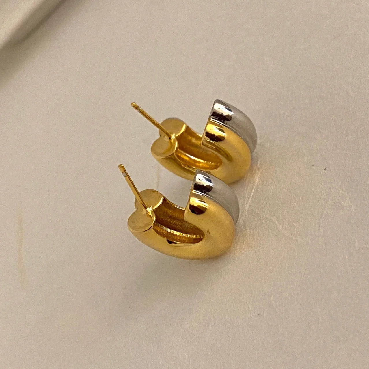 Nahaufnahme zweier dicker zweifarbiger (Gold und Silber) Creolen-Ohrringe mit Steckverschluss.