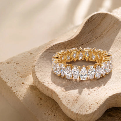 Prachtvoller Eternity-Damenring aus 14 Karat vergoldetem Silber mit rundum verlaufendem Tropfenschliff-Besatz auf beiger Deko-Schale