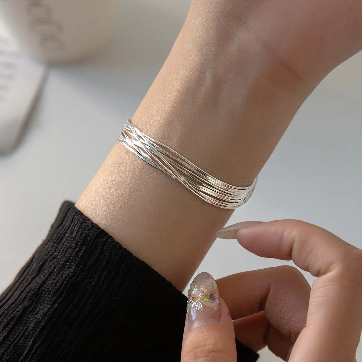 Elegante Trageansicht: Breites, mehrreihiges Silberarmband am Handgelenk einer Frau zu einem schwarzen Pullover
