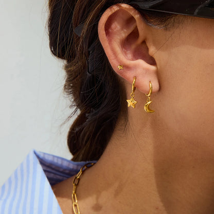 Das Ohr einer Frau von der Seite, das einen kleinen, goldenen Ohrstecker in Sternform aus Edelstahl mit 18K PVD-Vergoldung trägt.