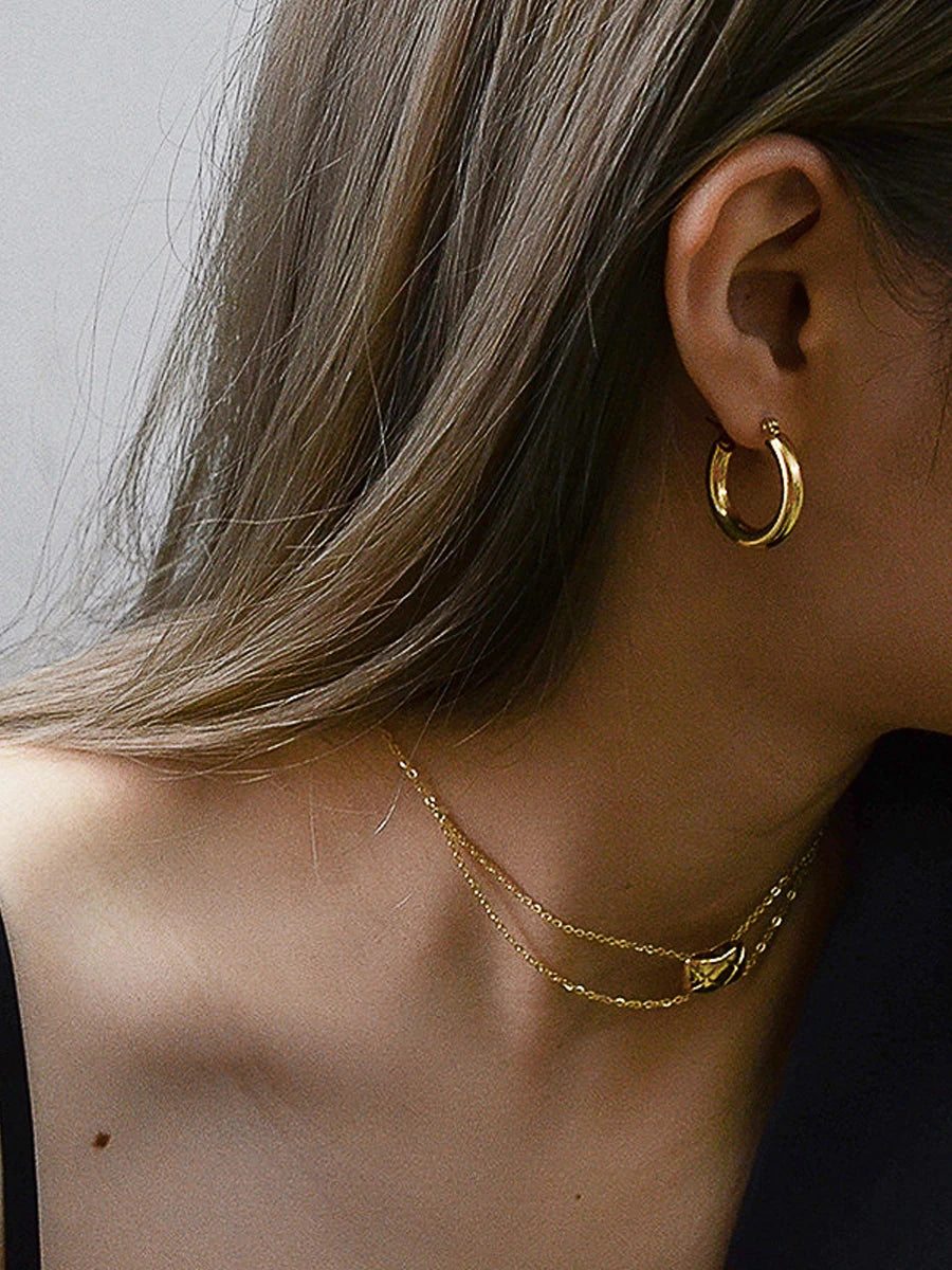 Nahaufnahme: Frau trägt glänzende, breite 18K vergoldete Creolen und feine Goldketten.