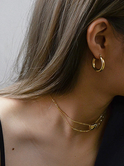 Nahaufnahme: Frau trägt glänzende, breite 18K vergoldete Creolen und feine Goldketten.