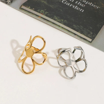 Die goldenen und silbernen Blumenringe liegen auf einem dunklen Buch und einer hellen Oberfläche. Die goldenen Ringe haben eine verdrehte Form, während die silbernen glatt sind.