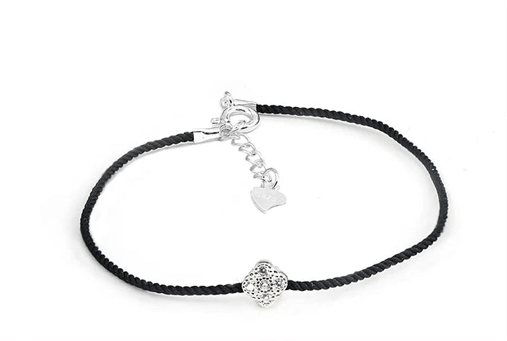 Nahaufnahme eines Armbands mit schwarzem Textilband und einem kleinen, runden Anhänger aus 925er Silber mit einem zentralen Zirkoniastein. Der Verschluss hat einen Herz-Anhänger aus 925er Silber.