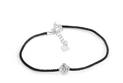 Nahaufnahme eines Armbands mit schwarzem Textilband und einem kleinen, runden Anhänger aus 925er Silber mit einem zentralen Zirkoniastein. Der Verschluss hat einen Herz-Anhänger aus 925er Silber.